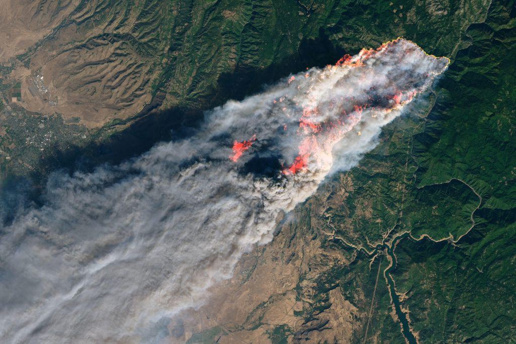 Aerial view of a California wildfire burning across forested hills